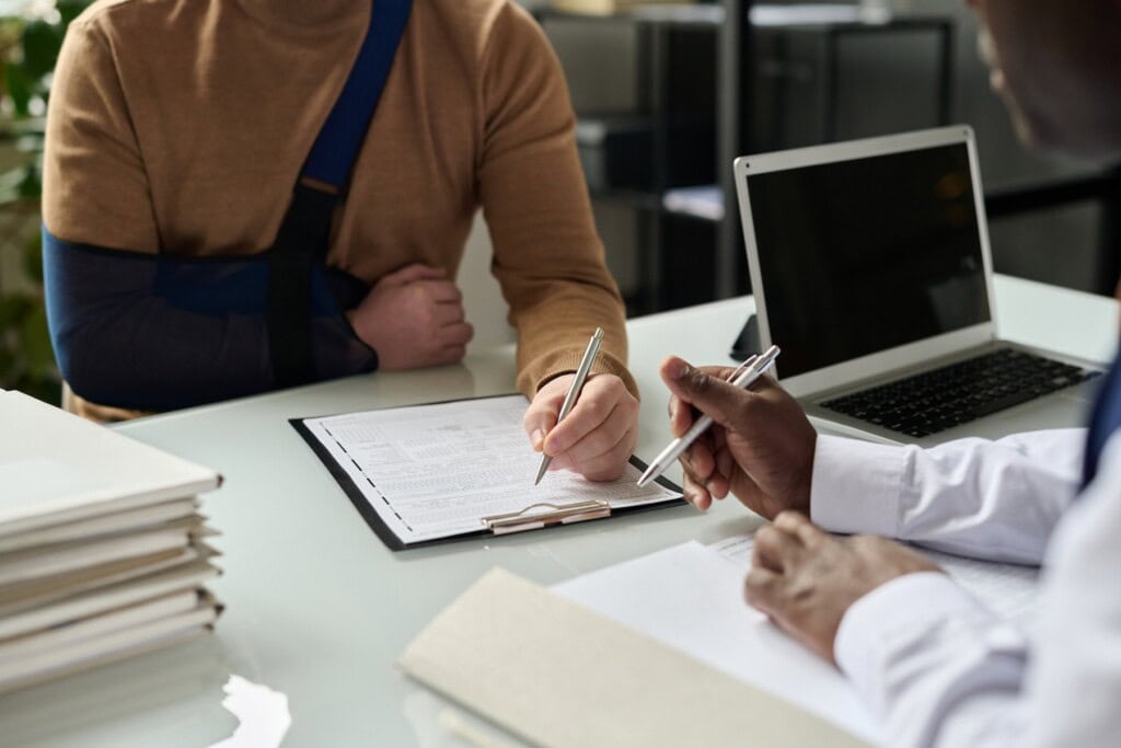 Man with injured hand in sling filling in legal paperwork with lawyer