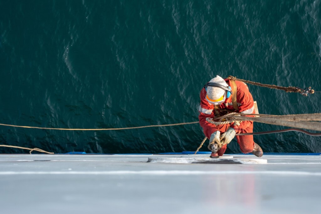 Seaman ship crew working aloft at height derusting and getting vessel ready for painting.