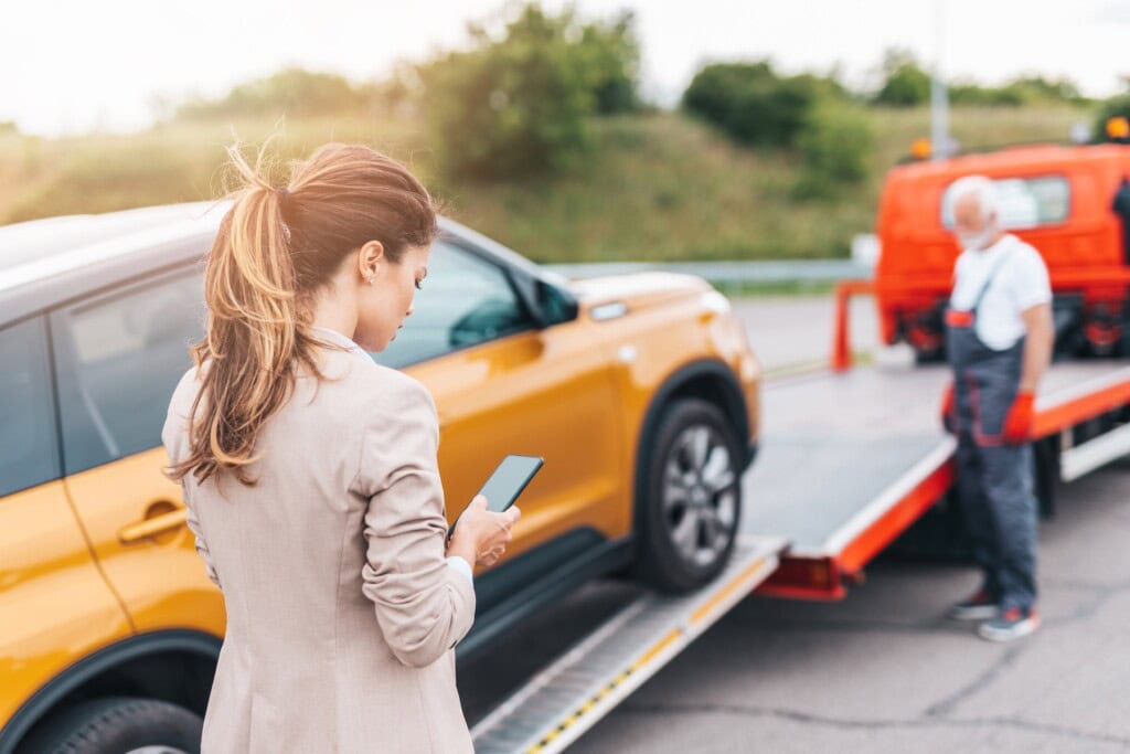 Woman in a suit looking using her cellphone as her car is towed