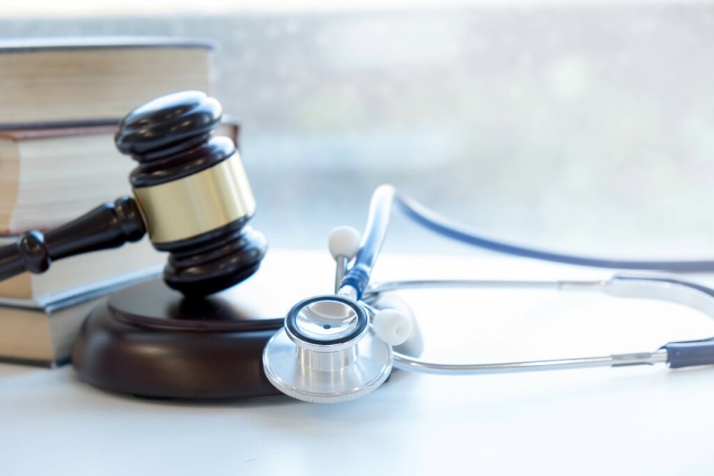 Judges gavel and medical stethescope on a white table next to a stack of books