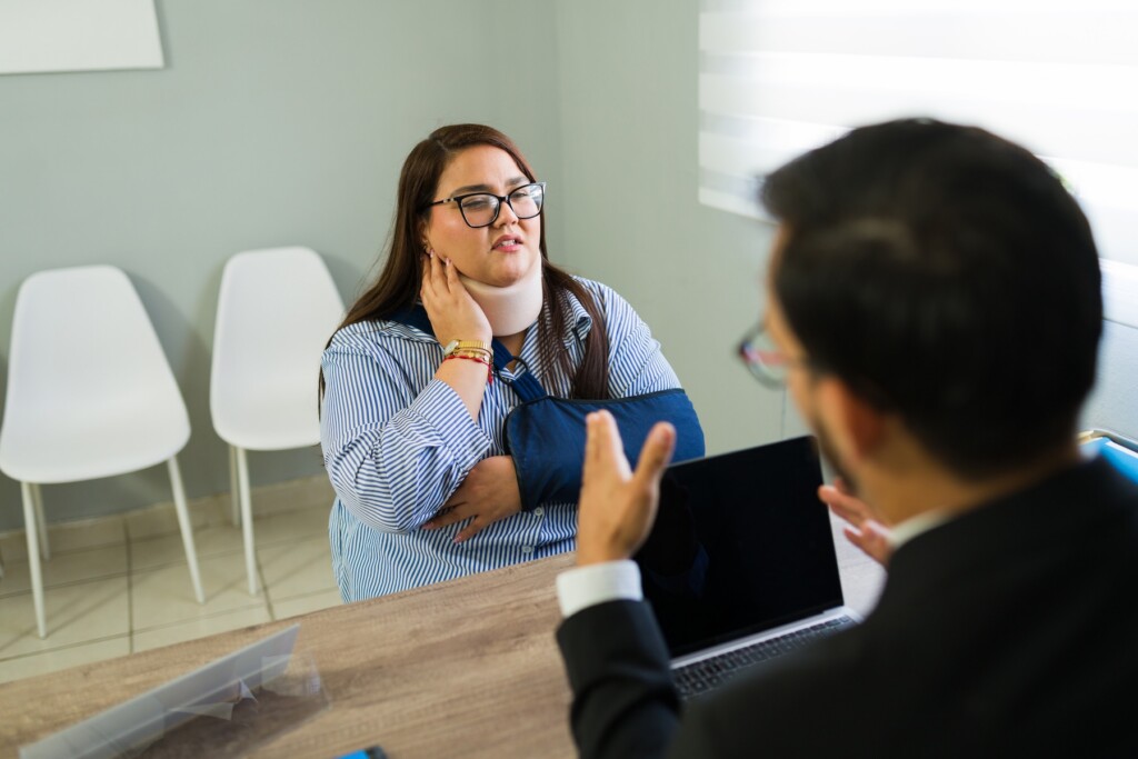 Woman with neck brace and arm sling consulting with a lawyer about her personal injury claim in a modern office setup