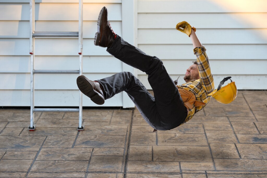 Worker with hard hat falling from ladder onto concrete floor